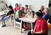 Flere personer sitter rundt et bord med kaffe og småting i et lyst rom.