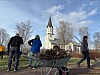 Personer samler kvist og løv i en trillebår foran en kirke.