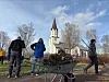 Personer samler kvist og løv i en trillebår foran en kirke.