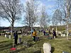 Personer rydder og arbeider blant gravsteiner på en kirkegård i solskinn.