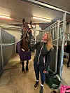 Brun hest i en oppselingsboks med kvinne som holder tøylene ved siden av.
