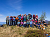Stor gruppe mennesker står samlet på et gresskledd fjell med hav og fjell i bakgrunnen.