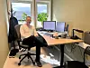 En mann sitter i en kontorstol ved et skrivebord med to skjermer i et lyst hjemmekontor.