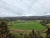 Grønne jorder og åser under overskyet himmel med kraftlinjer i forgrunnen.