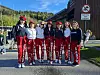 Gruppe stående utendørs på et torg med røde bukser og røde russeluer foran bygninger.