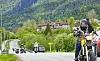 Motorsyklister kjører på en landevei med fjell og grønn vegetasjon i bakgrunnen.
