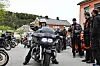 Motorsykkel i forgrunnen med flere andre sykler og personer samlet utenfor en bygning.