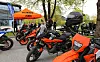 KTM-motorsykler parkert under et oransje telt ved en skogkledd veikant.