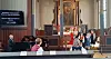 Et lite barnekor som synger foran alteret i en kirke med publikum på benker.