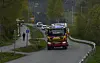 Brannbil på svingete vei med biler bak og skog på begge sider.