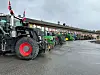 Flere traktorer står parkert på rekke ved en bygning på en våt parkeringsplass.