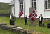 Tre personer står på gresset ved en hvit kirke og holder norske flagg.