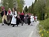 En gruppe barn og voksne går i tog langs en landevei med norske flagg.