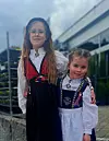 To barn i tradisjonelle festdrakter står sammen foran en bygning.