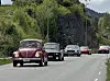 Flere biler kjører i kø på en vei gjennom et grønt landskap.