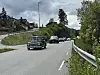 Gammel bil kjører foran andre biler på en vei med gress på begge sider.