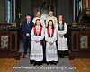 Fire festkledde ungdommer og to geistlige står oppstilt foran alteret i en kirke.