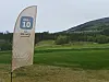 En høy markør står på en golfbane med grønne fairwayer og åser i bakgrunnen.