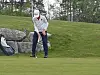 Golfer står bøyd over ballen på en golfbane med golfbag og trær i bakgrunnen.