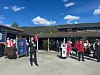 Gruppe av elever og ansatte står i skolegårdsrom med flagg og bygninger under blå himmel.