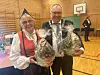 Dame i nordmørsbunad og mann med ordførerkjede står i en gymsal og holder store gavekurver pakket inn i cellofan.