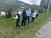 Barn trekker i et tau på gresset ved en vei med fjell i bakgrunnen.