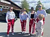 Fem personer i røde og hvite antrekk står utenfor en bygning, mens et barn står foran dem.