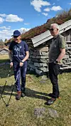 To personer står ute ved en steinbygning på en solrik dag.