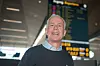 Smilende mann står i en flyplassterminal med avgangstavle i bakgrunnen.