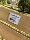 Trebenk med metallskilt merket Tindebekken i en park med trær og gress.