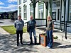 Tre personer står foran en hvitmalt bygning med grønne detaljer og en liten informasjonstavle ved inngangen.