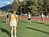 Personer spiller ball på en idrettsbane med kunstgress. Løpebane, trær og fjell i bakgrunnen.