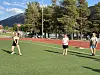 Tre personer spiller ball på en bane med kunstgress. Løpebane, trær og fjell i bakgrunnen.