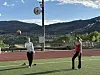 To personer på en bane med fjellandskap og himmel i bakgrunnen. En volleyball i luften.