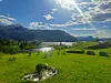 Grønn hage i forgrunnen med fjord og fjell i bakgrunnen under en solrik himmel.