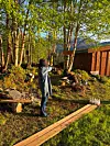Person med pil og bue sikter mot en målskive i en hage med trær og tregjerde.