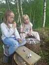To barn sitter utendørs i skogen og spiser is ved en benk og en trestubbe.