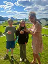 Tre personer på en gressplen med glass i hendene, med fjord og fjell i bakgrunnen.