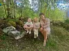 Tre personer sitter på en benk i en grønn skog med steiner og trær rundt dem.