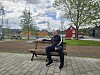 En mann sitter på en benk i en park med trær og små fargerike hus i bakgrunnen.