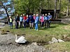 En gruppe personer står på en gressflate ved vannet, med en hvit svane foran dem.