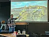 En mann peker på en projeksjon av en fjellsti med trapp og norsk tekst i et mørkt møterom.