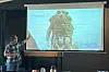 En mann peker mot en projektorvisning med bilde av en isbre på lerret i et mørkt rom.