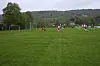 Fotballspillere på en stor gressbane med mål, trær og ås i bakgrunnen.