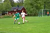 To ungdomsspillere utfordrer hverandre om ballen på en grønn fotballbane med mål i bakgrunnen.
