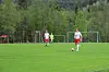 To fotballspillere på en grønn gressbane med ballen og skogkledd bakgrunn.