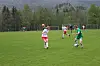 Flere fotballspillere løper etter ballen på en grønn bane med skog og fjell i bakgrunnen.