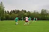 Fotballspillere i rødt og grønt spiller på en gressbane med trær i bakgrunnen.