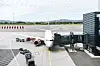 Passasjerfly ved gate med bagasjevogner og lasterampe på en kommersiell flyplass.