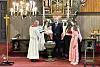 Prest og flere personer står foran alteret i en kirke med kors, lys og røde tepper.